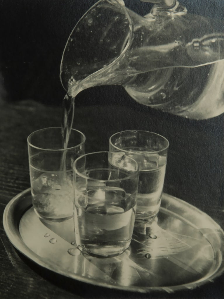 Wasser fließt aus einem Krug in drei Gläser